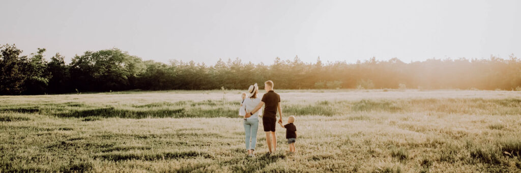 Eine Familie sieht sich auf einem Feld den Sonnenuntergang an.