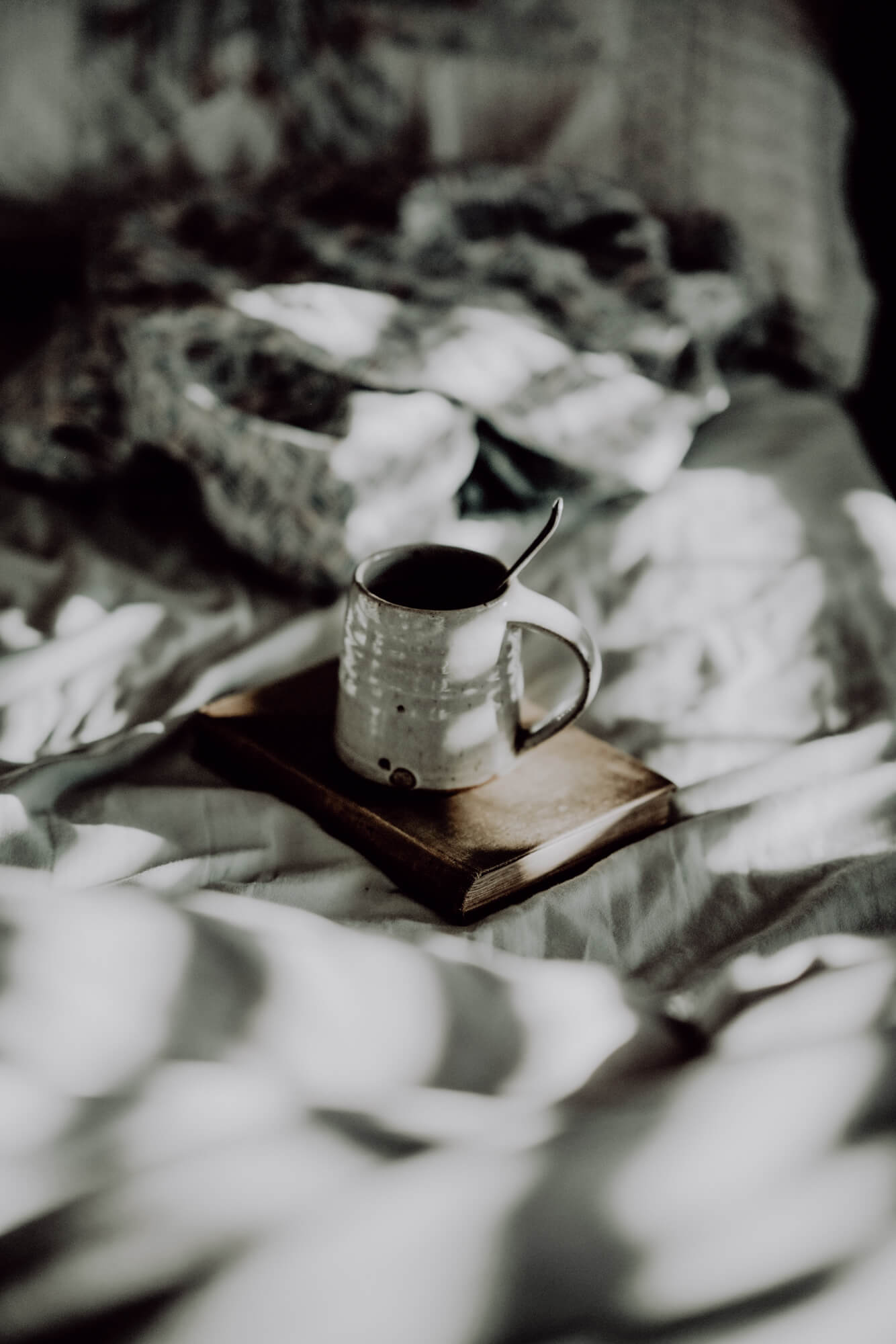 Eine graue Teetasse steht auf einem braunen Buchumschlag auf einer Bettdecke.